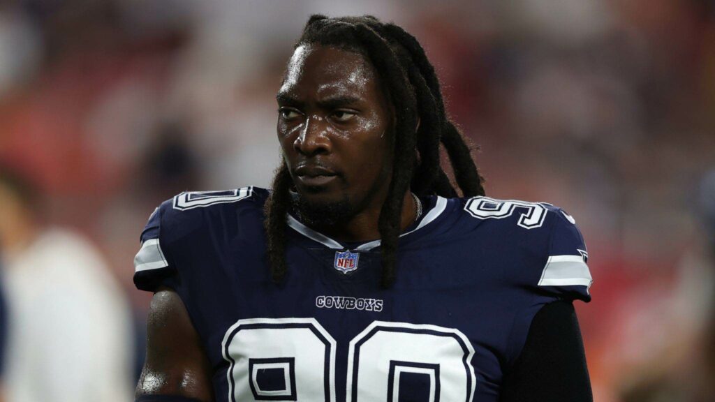 A football player in a navy blue "Cowboys" jersey with the number 90 is seen standing on the field.